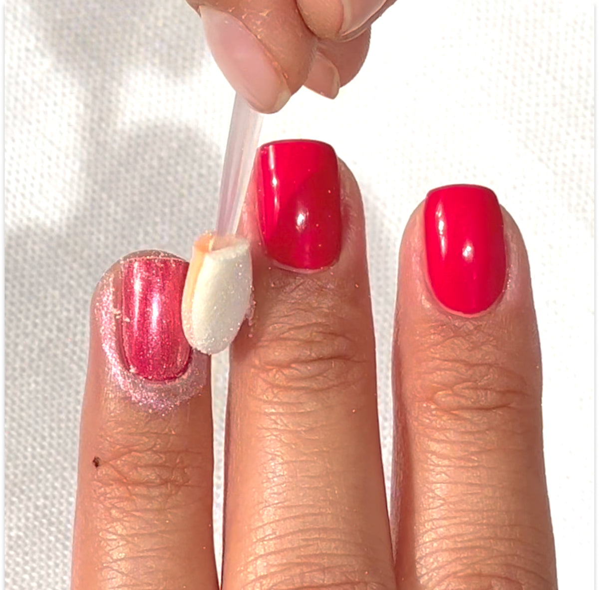 Une main avec du vernis à ongles rose vif est présentée. Un doigt est brossé avec un applicateur éponge, probablement pour appliquer des paillettes ou de la poudre sur l’ongle, tandis que les autres ongles restent intacts.