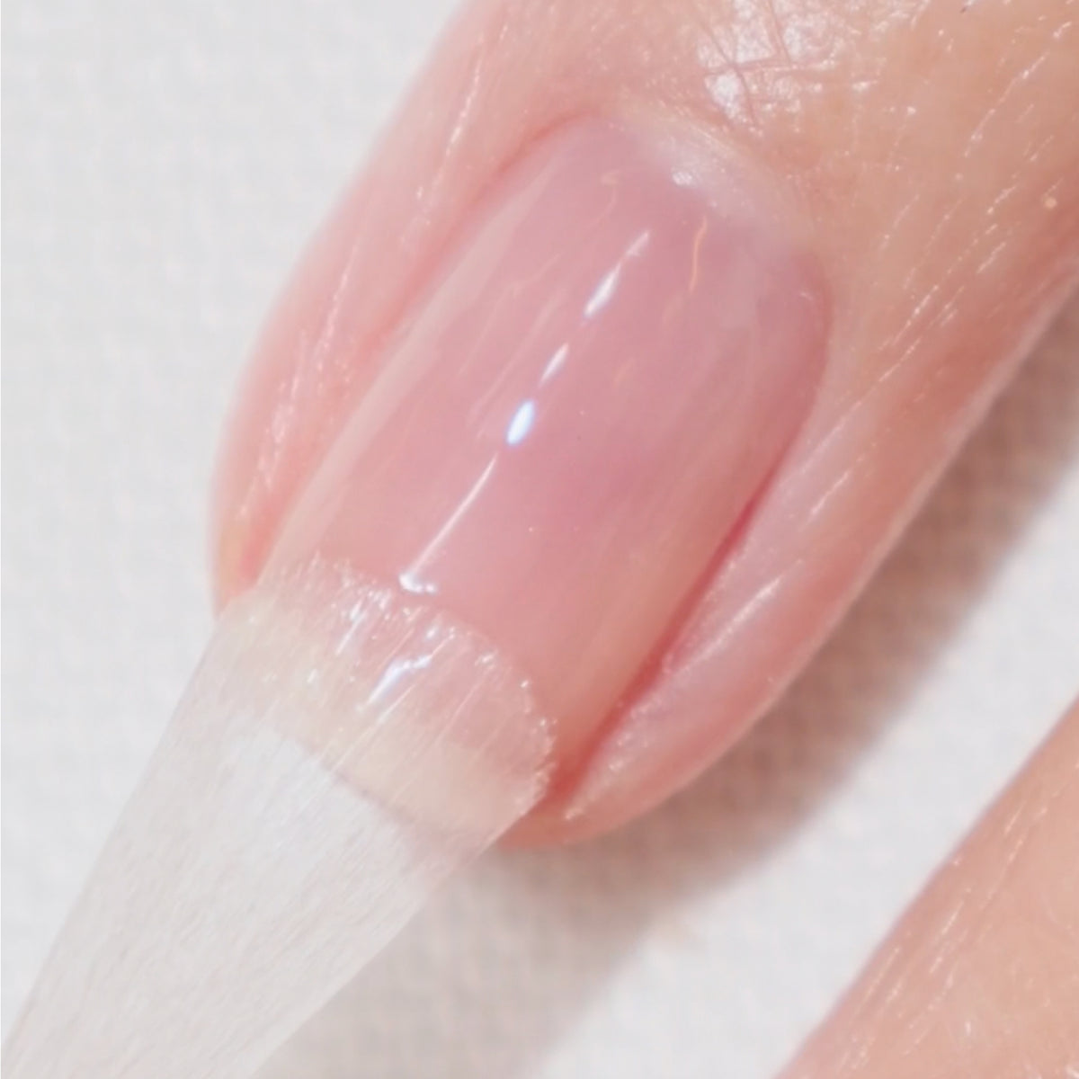 Gros plan d’un ongle en cours de pose de vernis transparent ou translucide, montrant le pinceau appliquant le vernis sur l’ongle naturel.