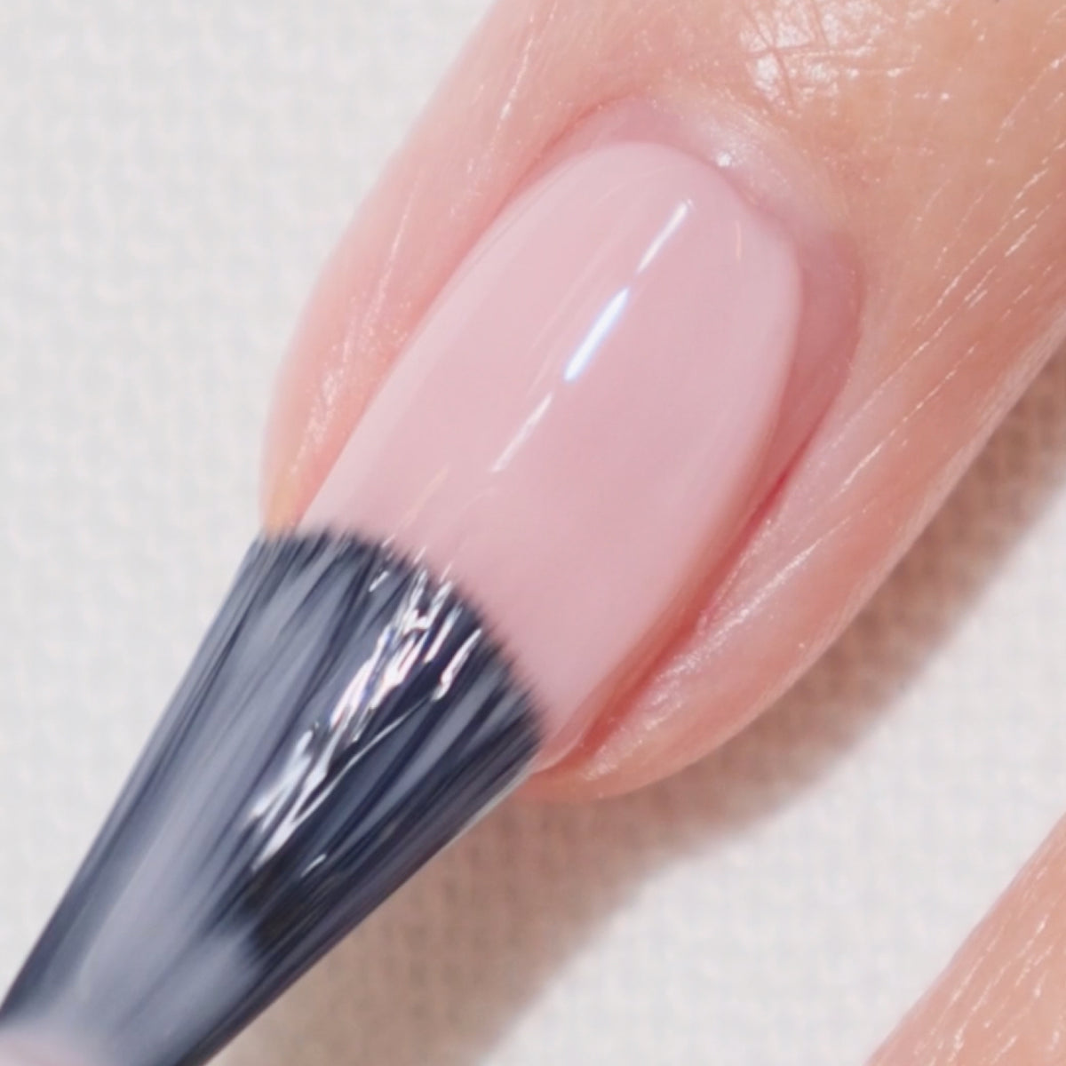 Gros plan d'un ongle en cours de pose de vernis à ongles rose clair au pinceau.