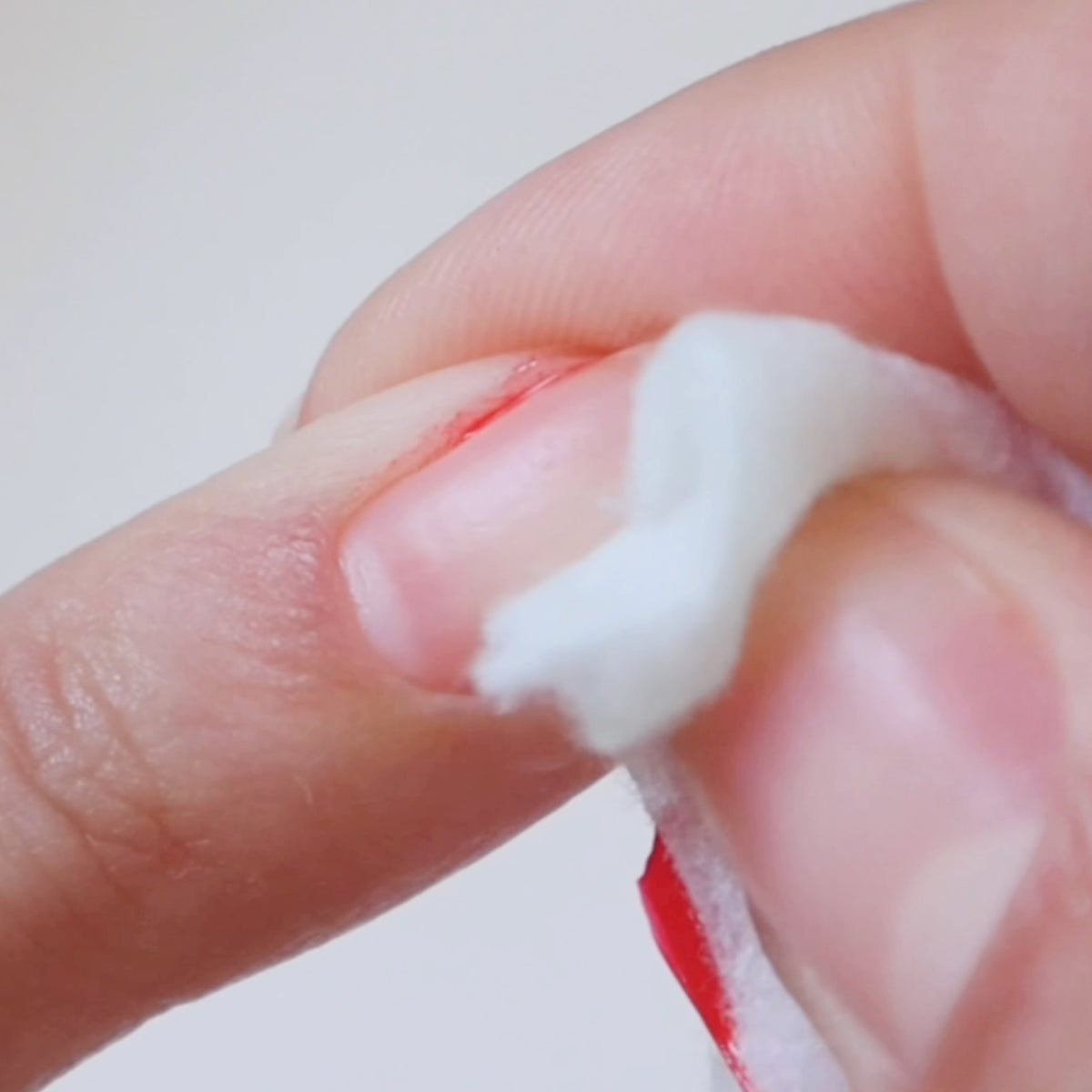 A close-up of a person using a cotton pad to clean around their fingernail, with a hint of red at the nails edge, possibly from nail polish or a small injury.