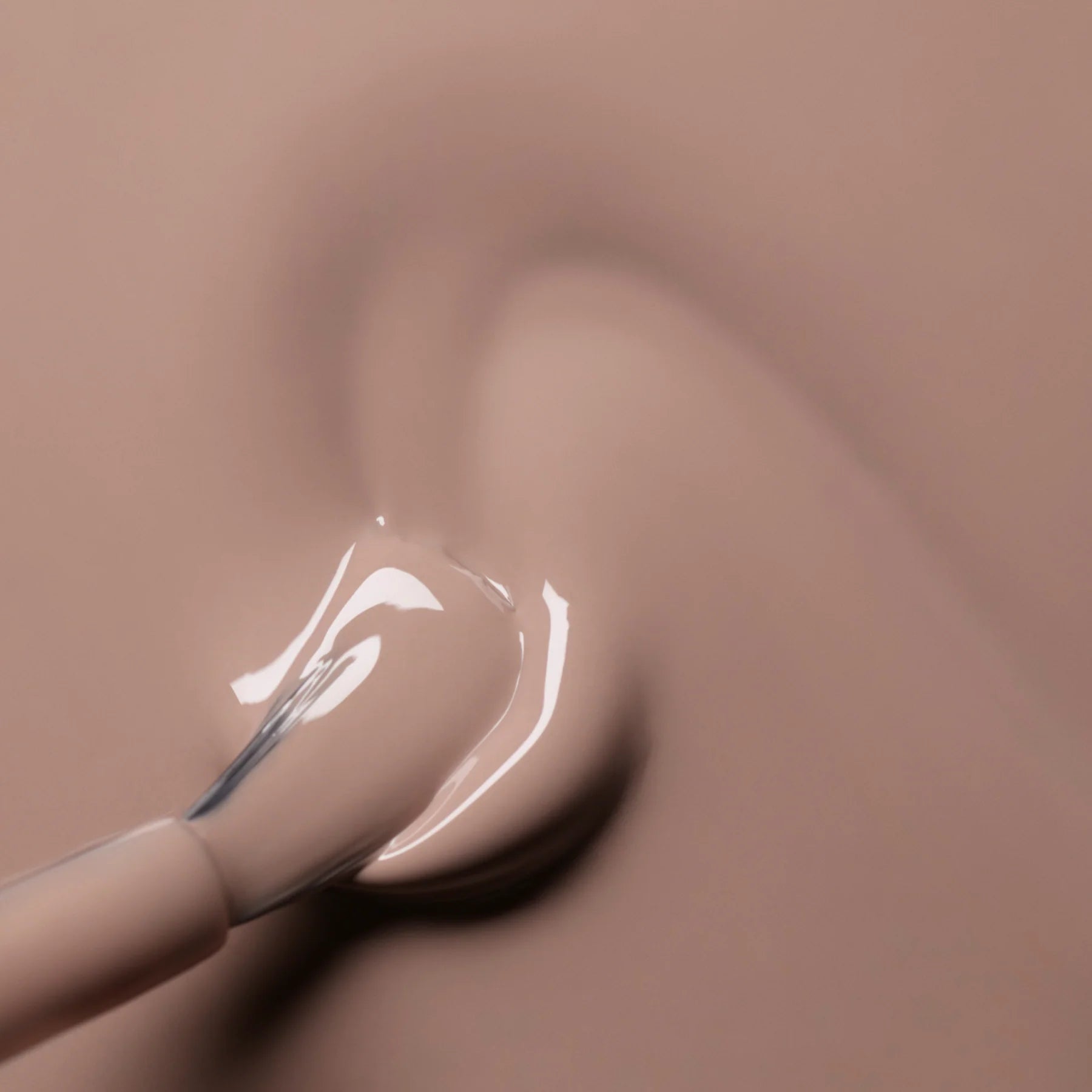 A close-up of a nail polish brush spreading light beige nail polish onto a smooth surface, creating a glossy and creamy texture.