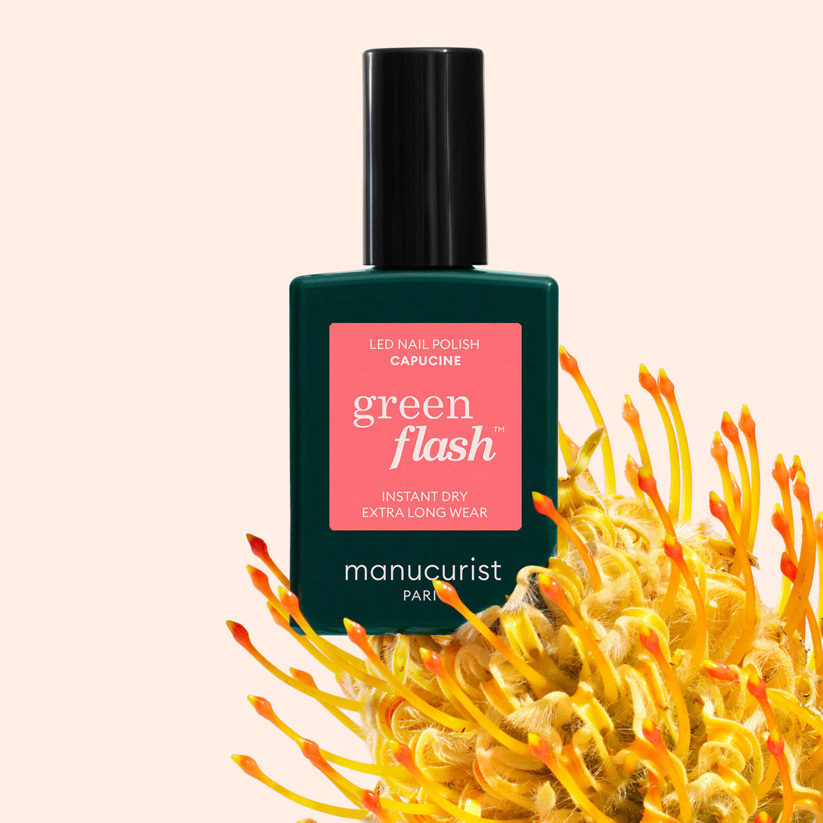 Un flacon de vernis gel Green Flash Capucine Manucurist est posé au milieu de fleurs jaune orangé sur un fond rose clair. L&