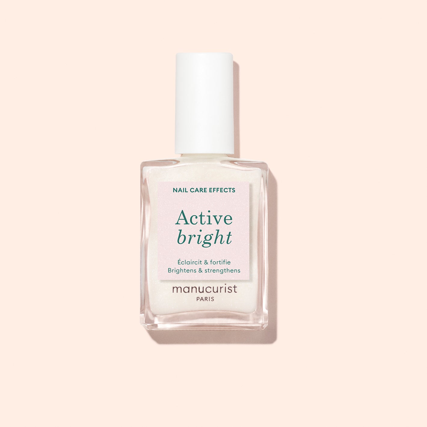 A clear glass bottle of Manucurist Active Bright nail care treatment with a white cap sits against a pale pink background. The label notes this bio-based formula as both a nail brightener and strengthener.