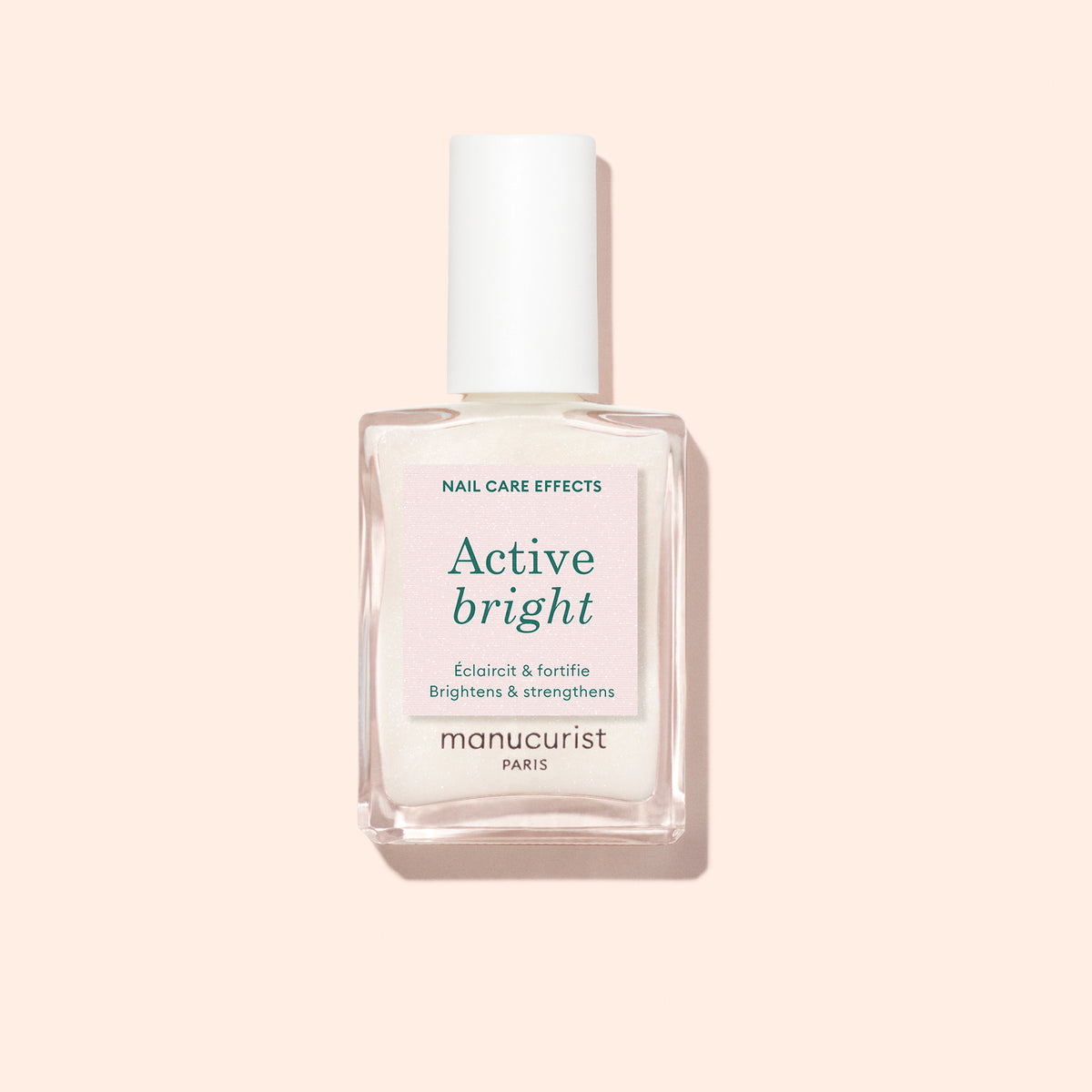 Un flacon en verre transparent de vernis à ongles Manucurist Active™ Bright, doté d’un bouchon blanc et placé sur un fond beige clair. L’étiquette indique que ce soin des ongles biosourcé illumine et renforce les ongles.