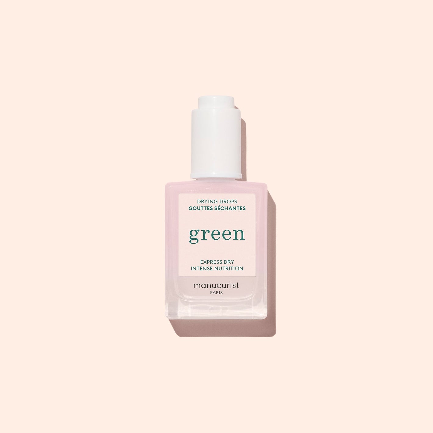 A square bottle of Manucurist Drying Drops with a white cap, featuring light pink liquid, is shown against a pale pink background. This nail product speeds up drying time and nourishes cuticles.