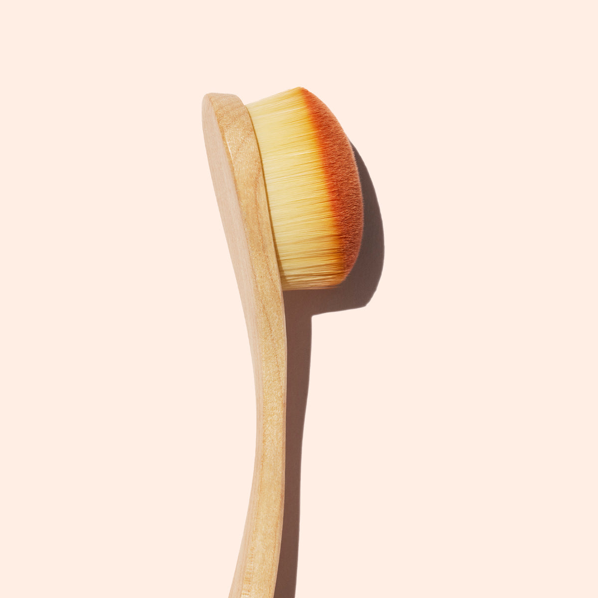 Le Dust Brush Manucurist présente un manche en bois, des poils véganes clairs et denses, ainsi qu’une tête légèrement arrondie, idéale pour le soin de la manucure, sur un fond beige pâle.