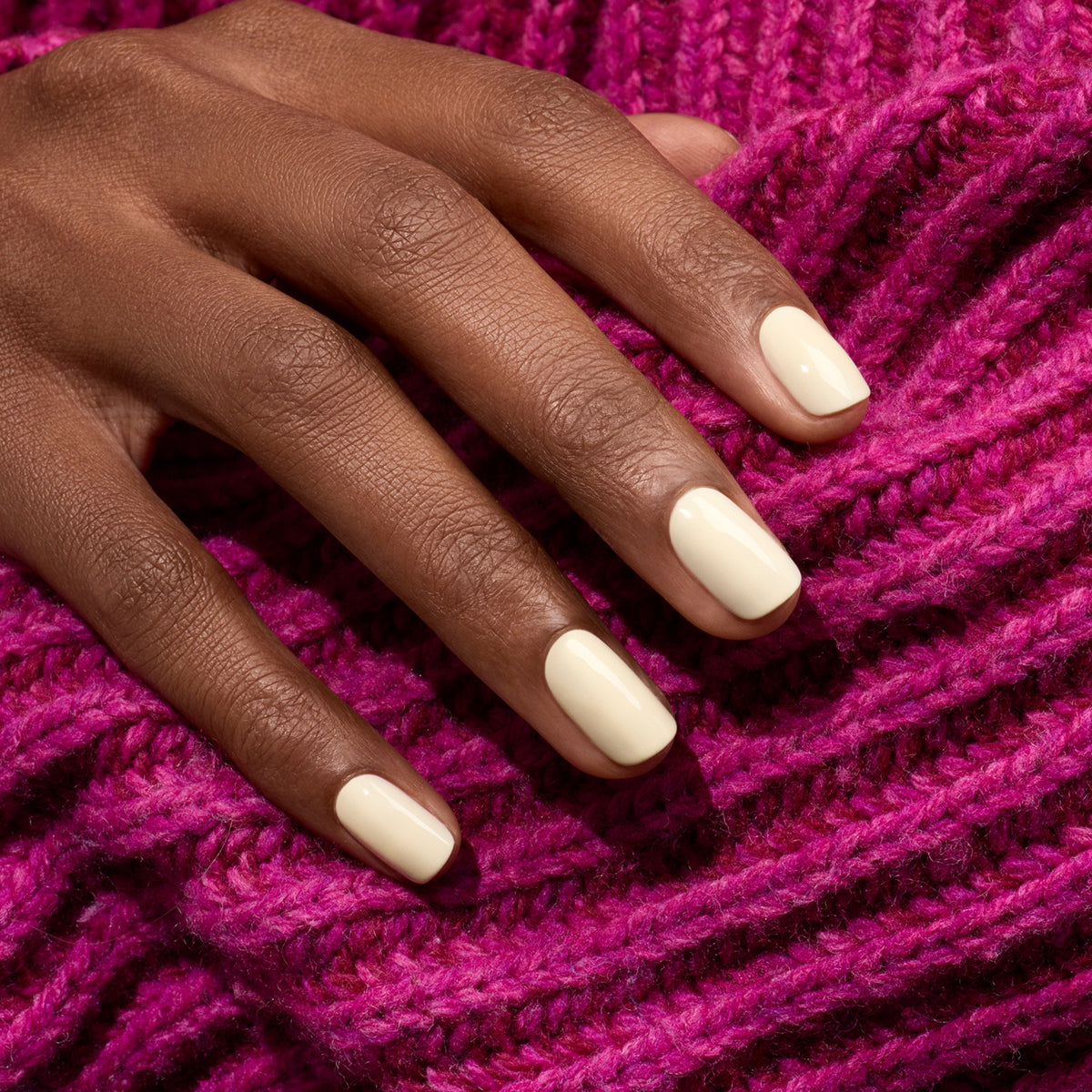 A hand with neatly manicured nails painted in Manucurist’s Shell, a minimalist off-white polish, rests on textured bright pink knit fabric.