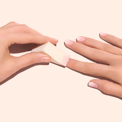 A hand uses Manucurist Nail Art Sponges (x4) to blend light pink polish, creating soft Baby Boomer nails on the other hand against a pale background.