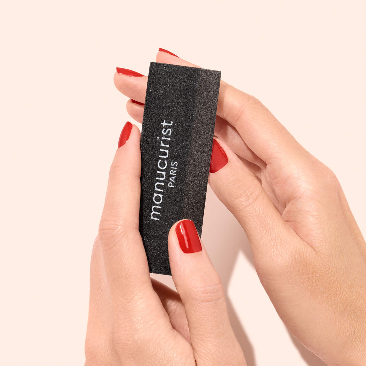 Des mains aux ongles manucurés rouges tiennent un bloc de dépose rapide noir et rectangulaire de Manucurist-us.