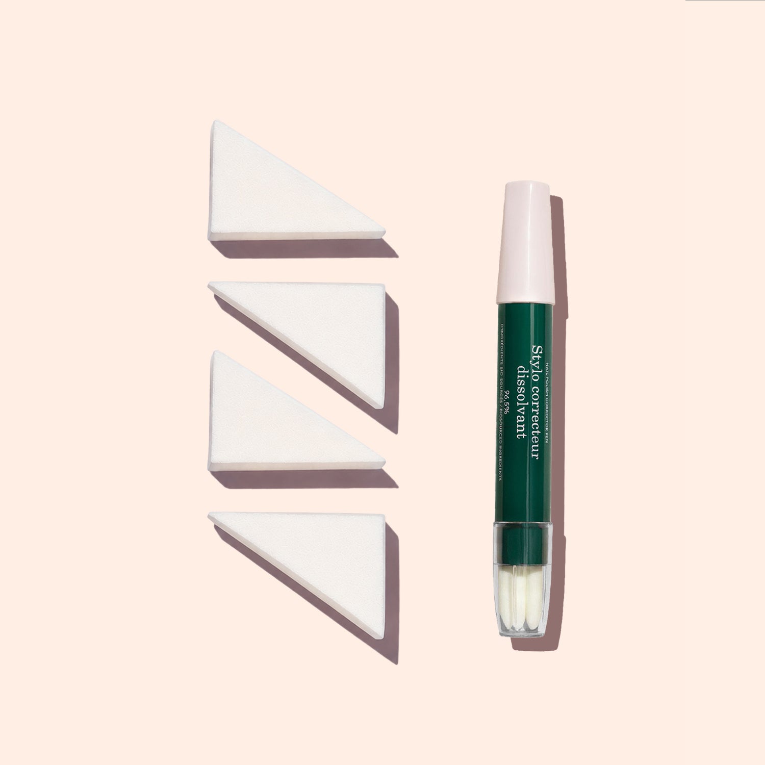 A green and pink capped makeup brush stands upright next to three Manucurist Nail Art Sponges (set of 4) arranged in a row on a light beige background.