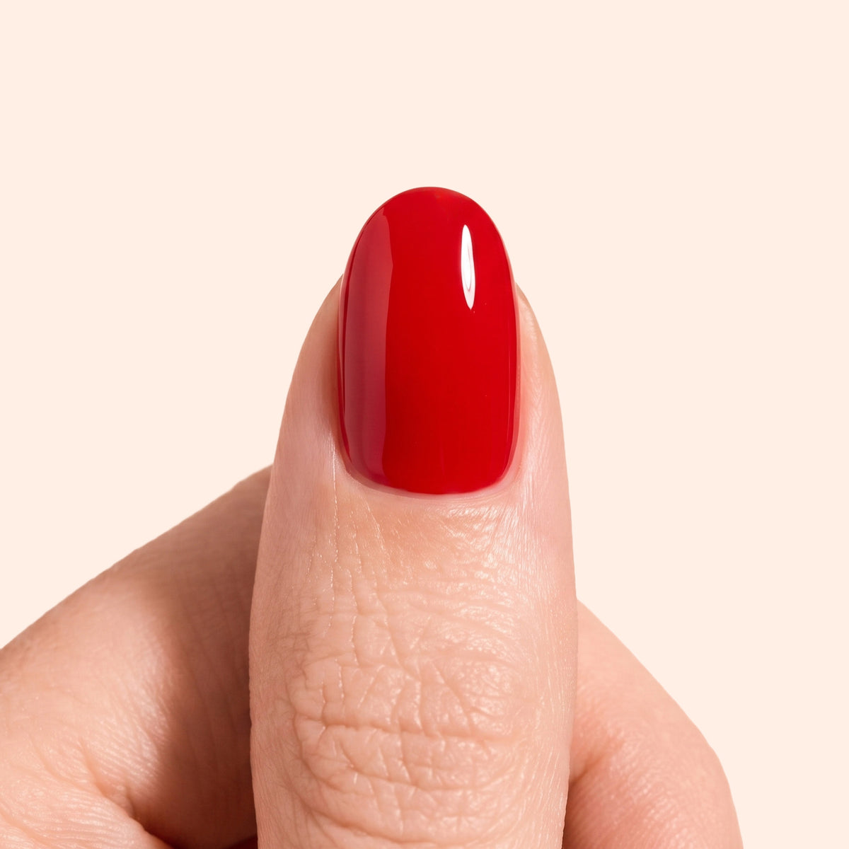 A close-up of a thumb with smooth, shiny red nail polish against a plain light background.