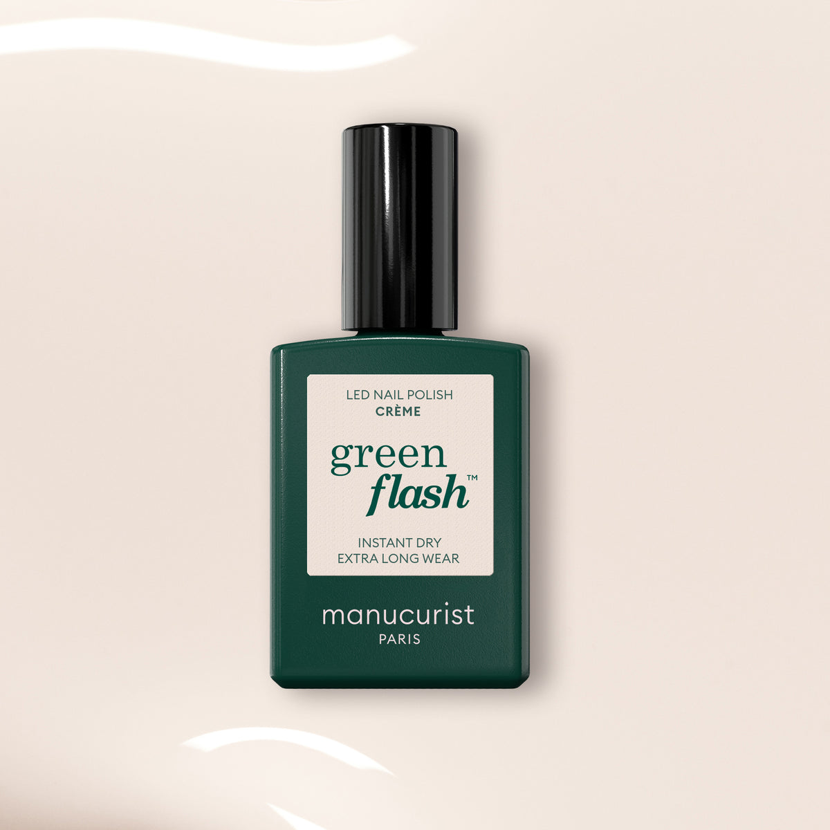 Un flacon de vernis gel Crème Manucurist dans un flacon rectangulaire vert foncé avec un bouchon noir, posé à la verticale sur un fond beige clair avec des reflets de lumière blanche.