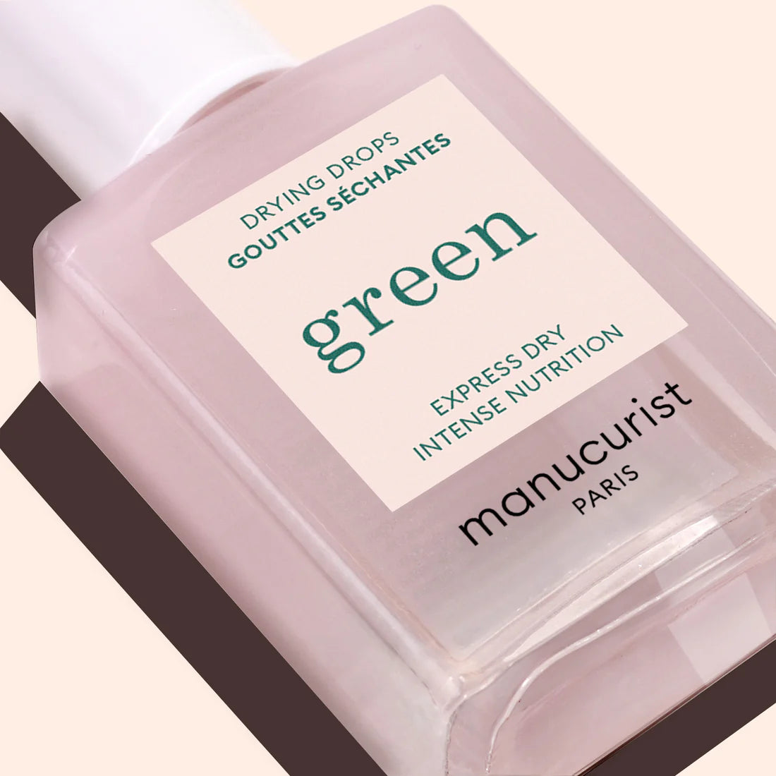 Un gros plan sur les Gouttes Séchantes Manucurist (Drying Drops), étiquetées en anglais et en français, promettant un séchage express et une nutrition intense pour des cuticules nourries, présentées sur un fond beige clair.