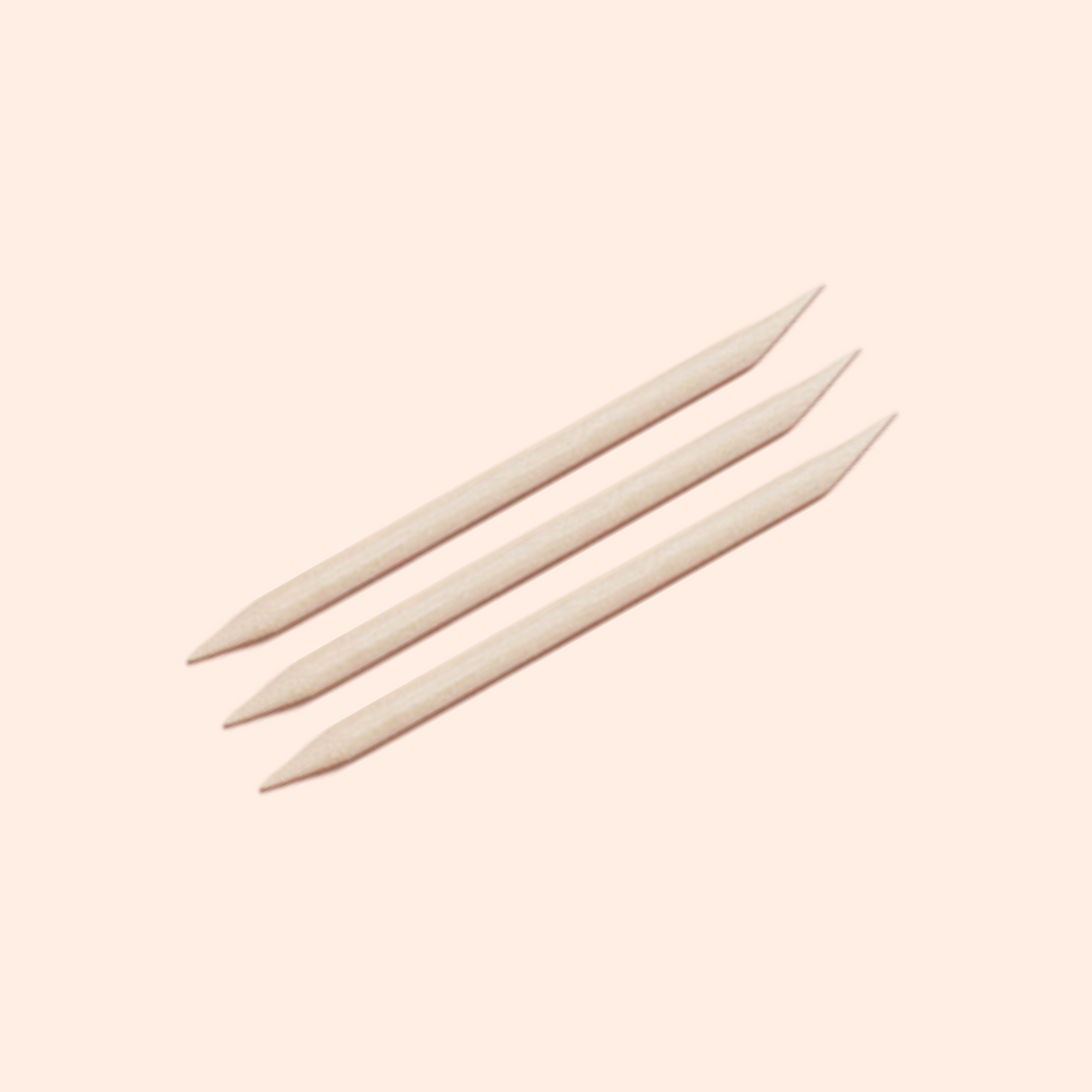 Two Manucurist US Wooden Cuticle Sticks, featuring pointed and angled ends, are arranged diagonally on a plain light beige background.