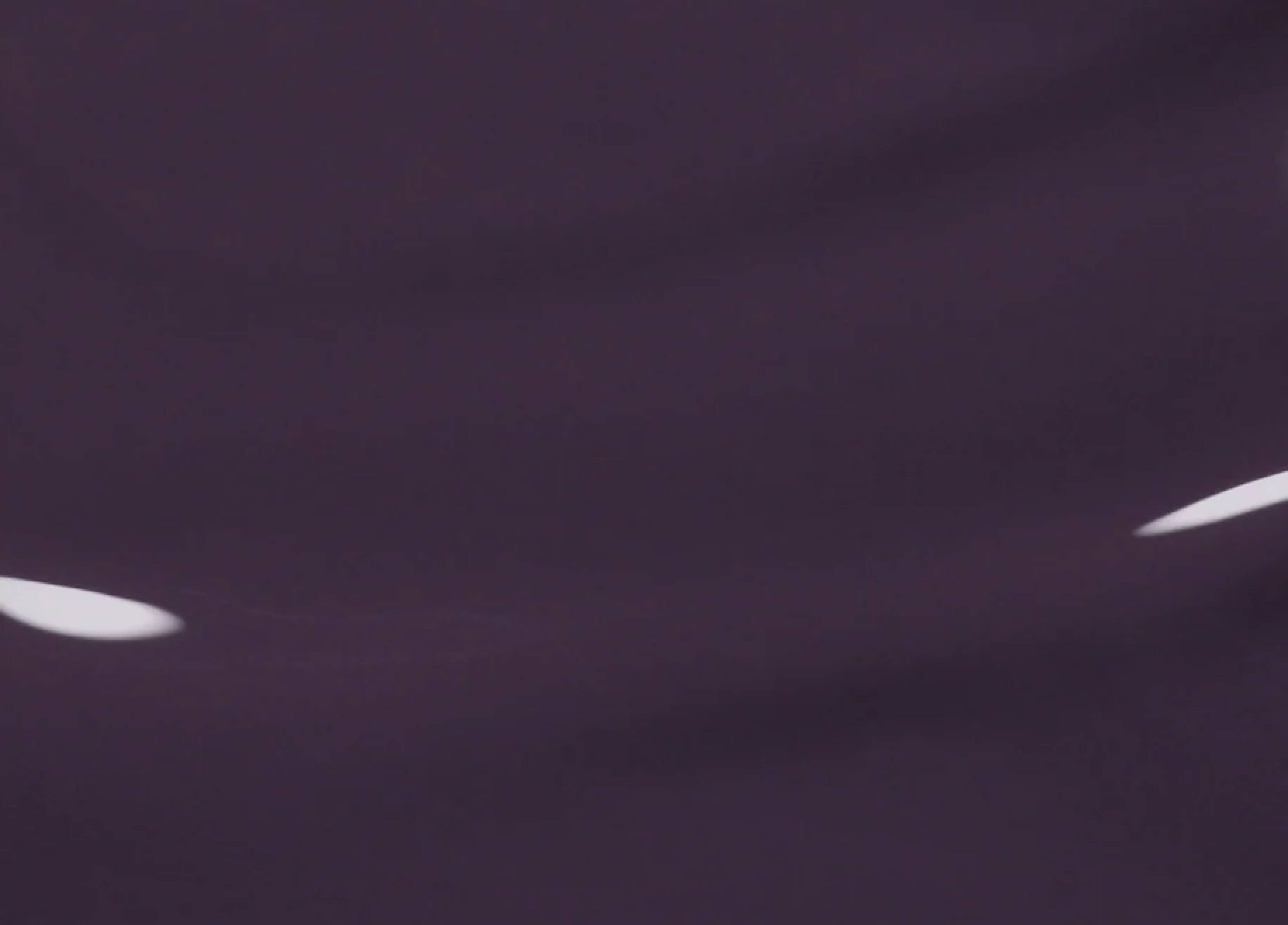 A close-up image of a dark, smooth surface with two white, curved light reflections on it. The background appears to be a deep shade of purple or black.