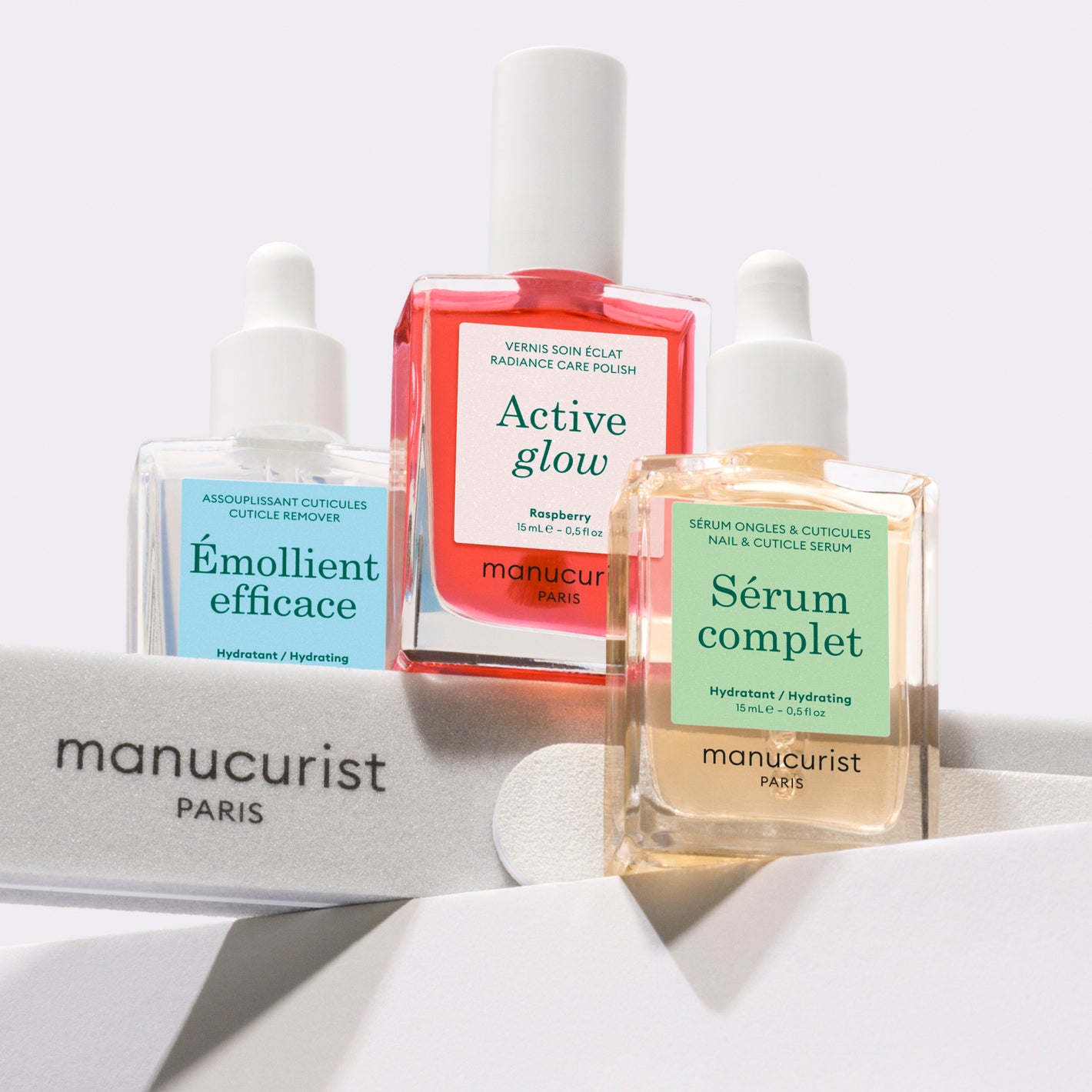 Three manicure product bottles labeled Émollient efficace, Active glow, and Sérum complet by Manucurist Paris, displayed on white nail files against a light background.