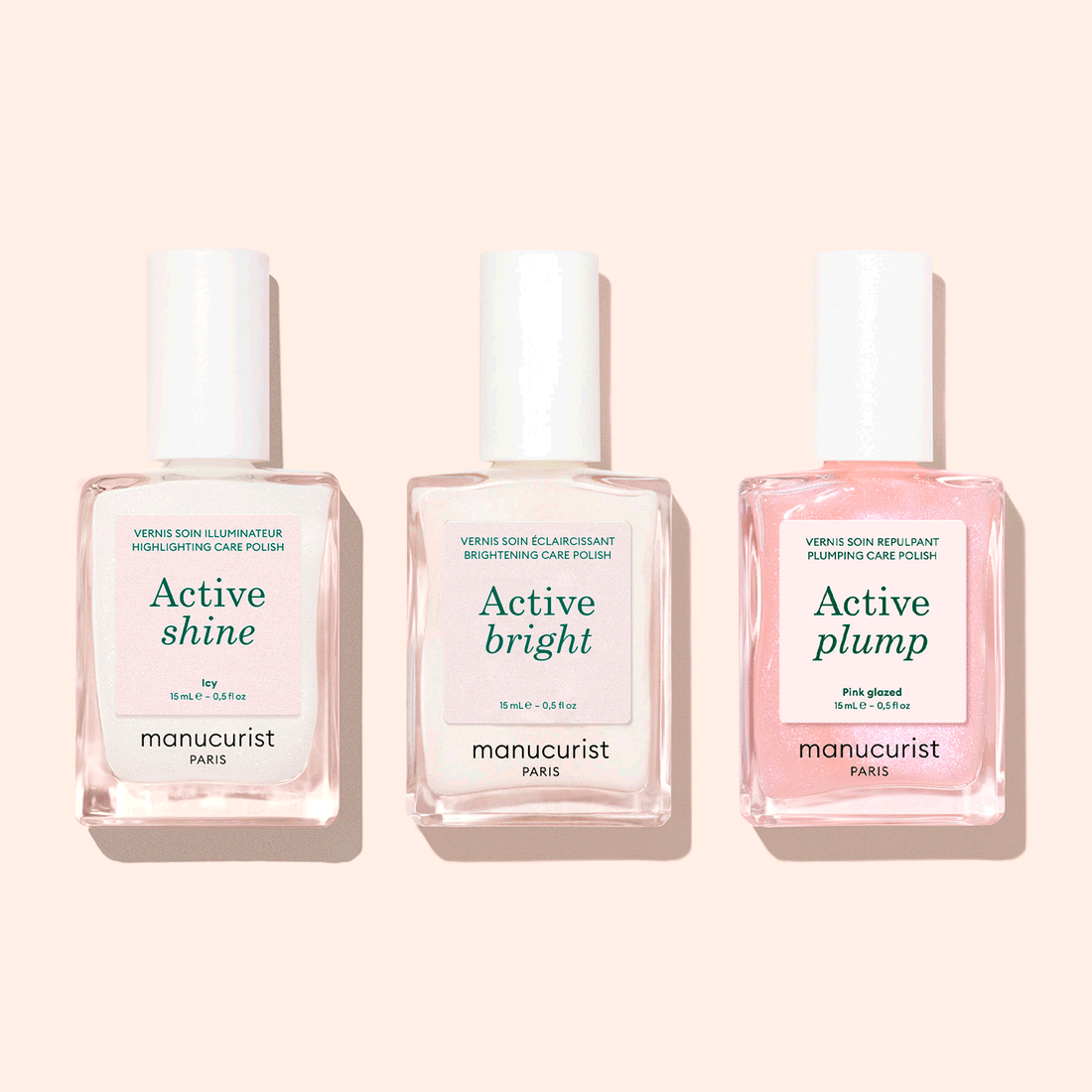 Three glass bottles from the Manucurist Customizable Active™ Trio—labeled Active Shine, Active Bright, and Active Plump—stand side by side on a pale pink background. These nail care polishes feature pale pink and clear shades, ideal for achieving a personalized look with natural makeup effects.