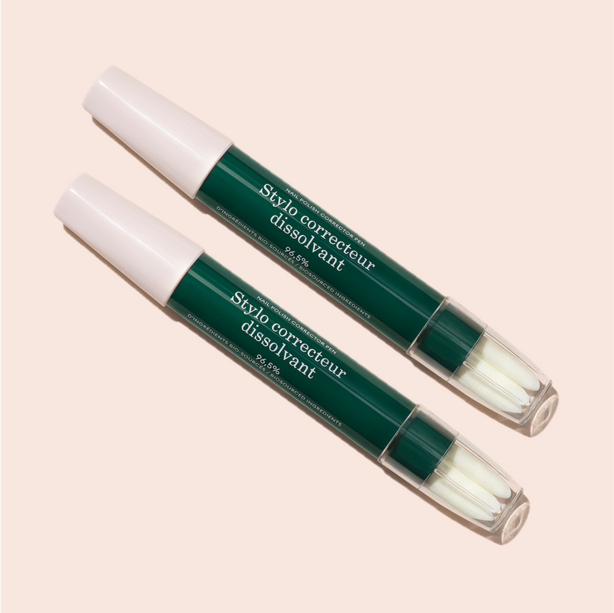Deux stylos correcteurs de vernis Manucurist-test [Test jauge] verts et blancs avec capuchons transparents, étiquetés "Stylo correcteur dissolvant", sont disposés en diagonale sur un fond beige clair — parfaits pour des retouches de vernis semi-permanent précises.
