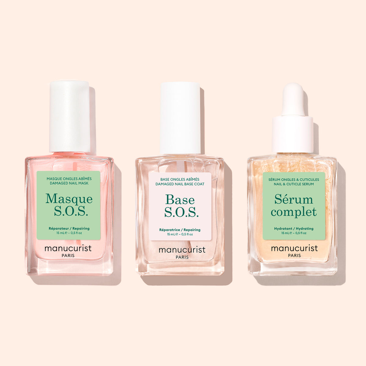 Trois flacons en verre transparent avec des bouchons blancs, étiquetés S.O.S. Nail Mask de Manucurist, sont disposés côte à côte sur un fond beige clair.