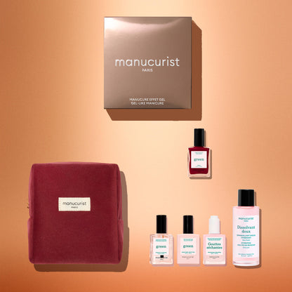 Flat lay of the Manucurist Green™ Discovery Kit Gift Set, featuring a burgundy pouch, a brown Manucurist box, a red gel effect manicure nail polish, and bottles of naturally derived nail polishes and nail care products on a gradient peach background.