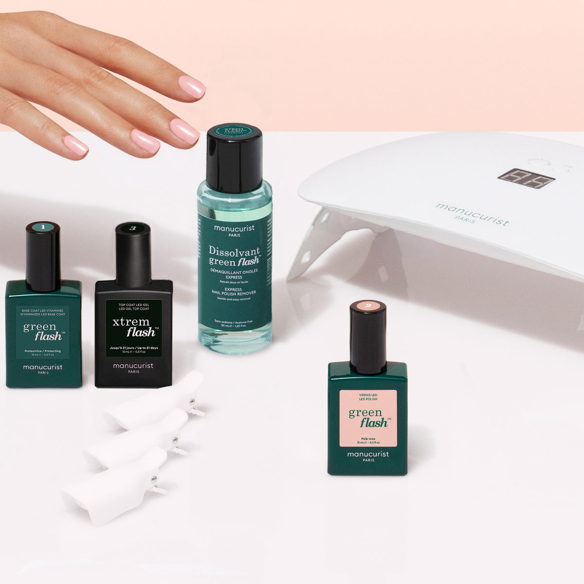 A hand with pink manicured nails hovers over a Manucurist Discovery Kit - Soap Nails LED Gel Polish, containing three bottles of gel polish, a bottle of remover, two nail clips, and an LED lamp.