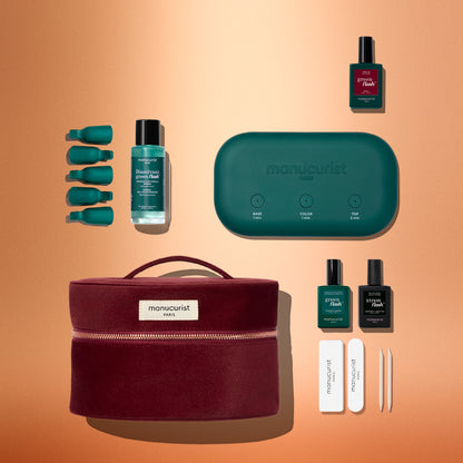 Le coffret kit découverte Green Flash™ de Manucurist réunit une élégante trousse en velours rouge, une lampe turquoise, des vernis effet gel, des soins essentiels pour les ongles, des limes et des accessoires pour les cuticules, soigneusement disposés sur un fond orange. Tout le nécessaire pour une manucure digne d’un salon à la maison.