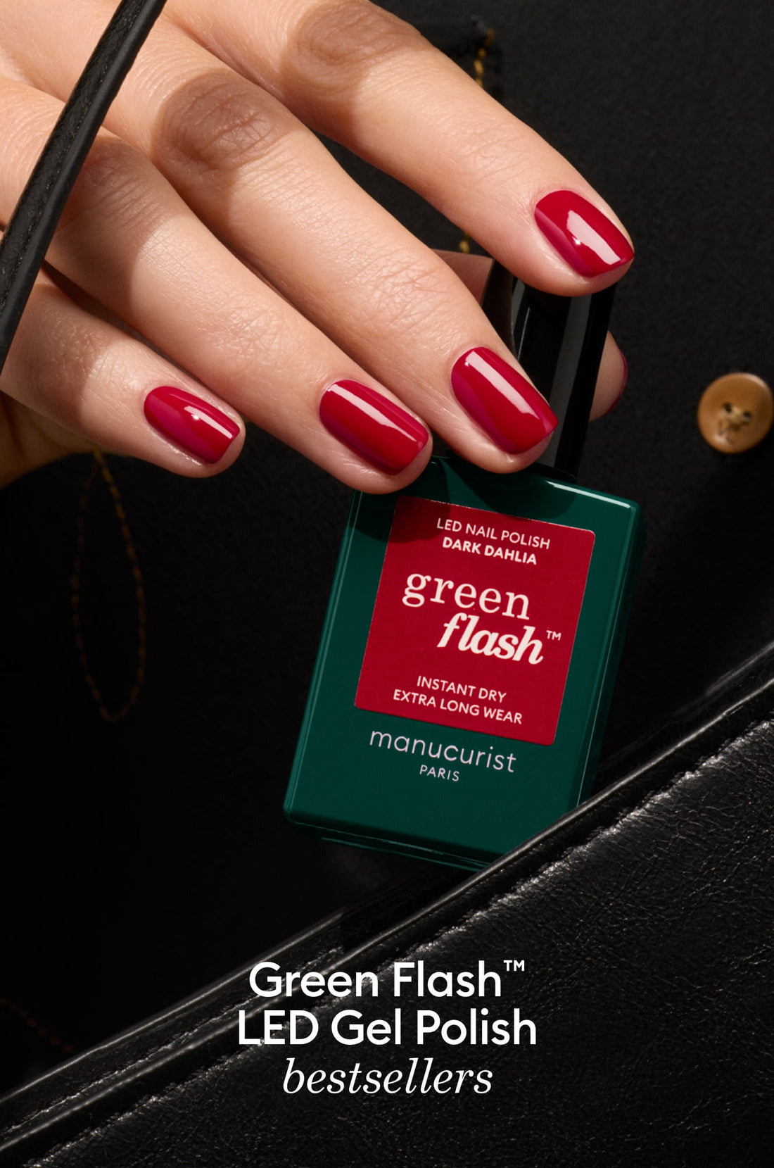A hand with glossy, deep red nails holds a bottle of Green Flash LED gel polish in the shade Dark Dahlia against a black background. The text reads: Green Flash LED Gel Polish bestsellers.