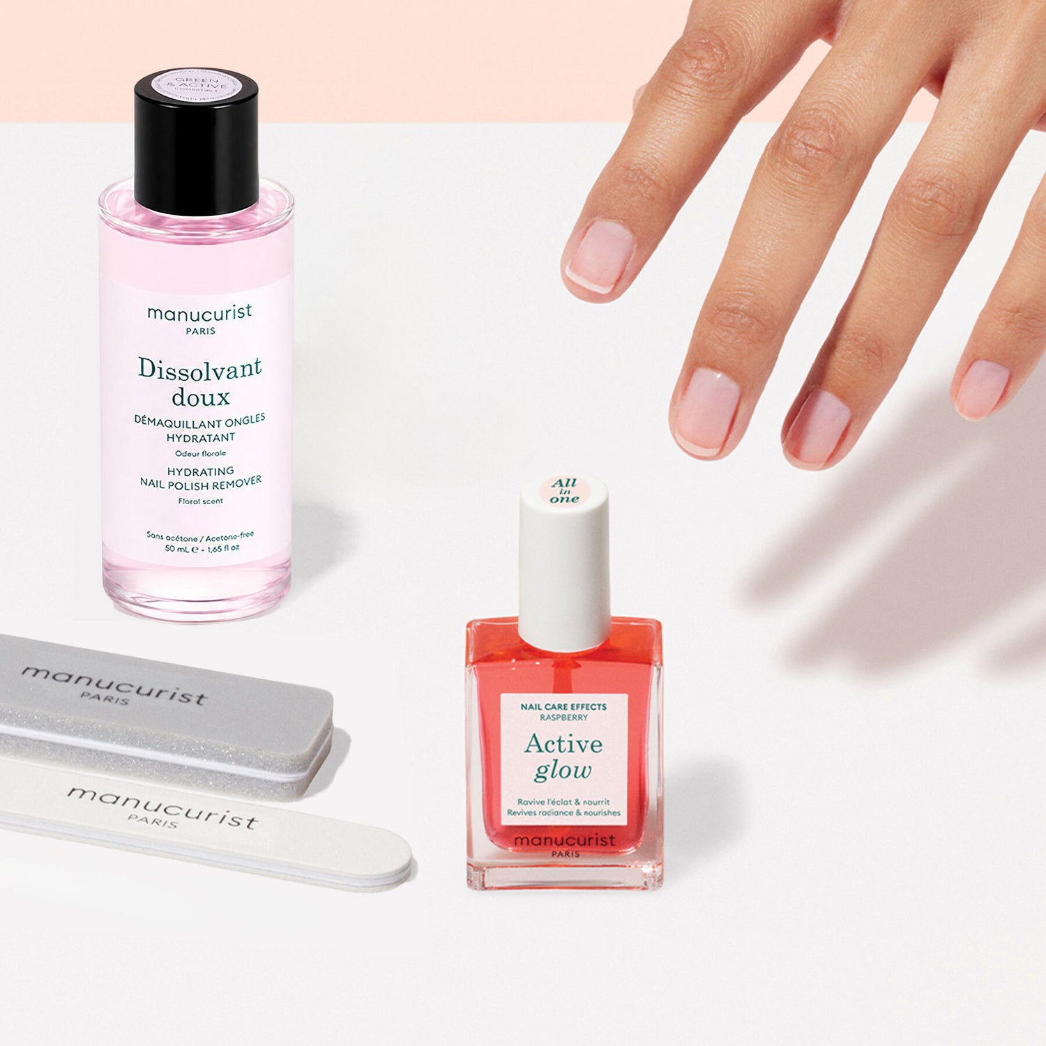 A hand with manicured nails is reaching toward the Manucurist Active Discovery Kit, featuring nail care essentials like nail polish remover, nail polish, and nail files—all arranged on a light surface—perfect for hydrating nails and cuticles as part of your flawless manicure routine.