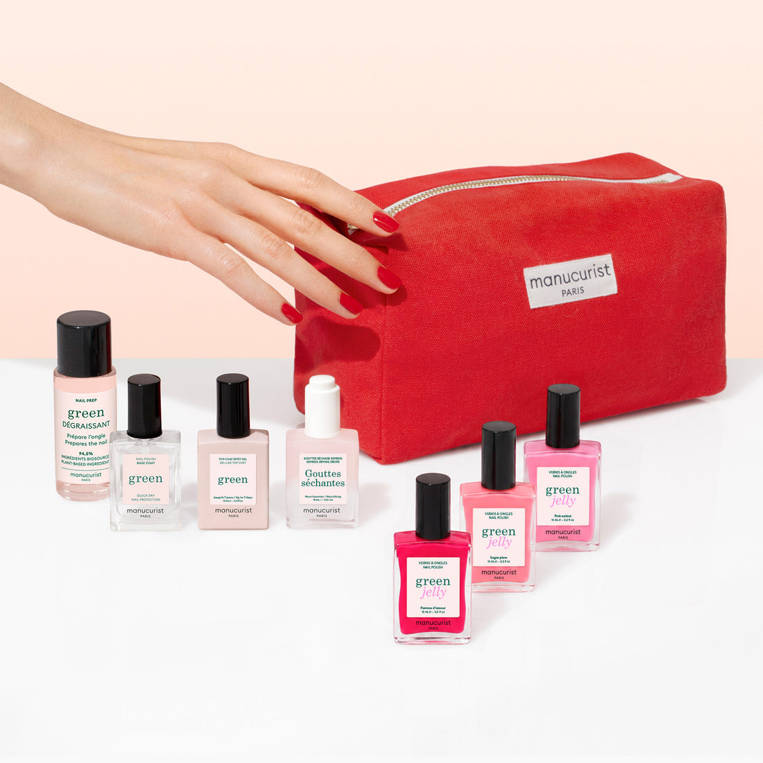 A hand with red nails reaches for a Starter Kit - Jelly Nail Polish pouch from Manucurist, surrounded by various Manucurist nail care products—highlighting the power of plant-based formulas for achieving the perfect Green manicure.