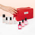 A hand with red nails reaches for a Starter Kit - Jelly Nail Polish pouch from Manucurist, surrounded by various Manucurist nail care products—highlighting the power of plant-based formulas for achieving the perfect Green manicure.