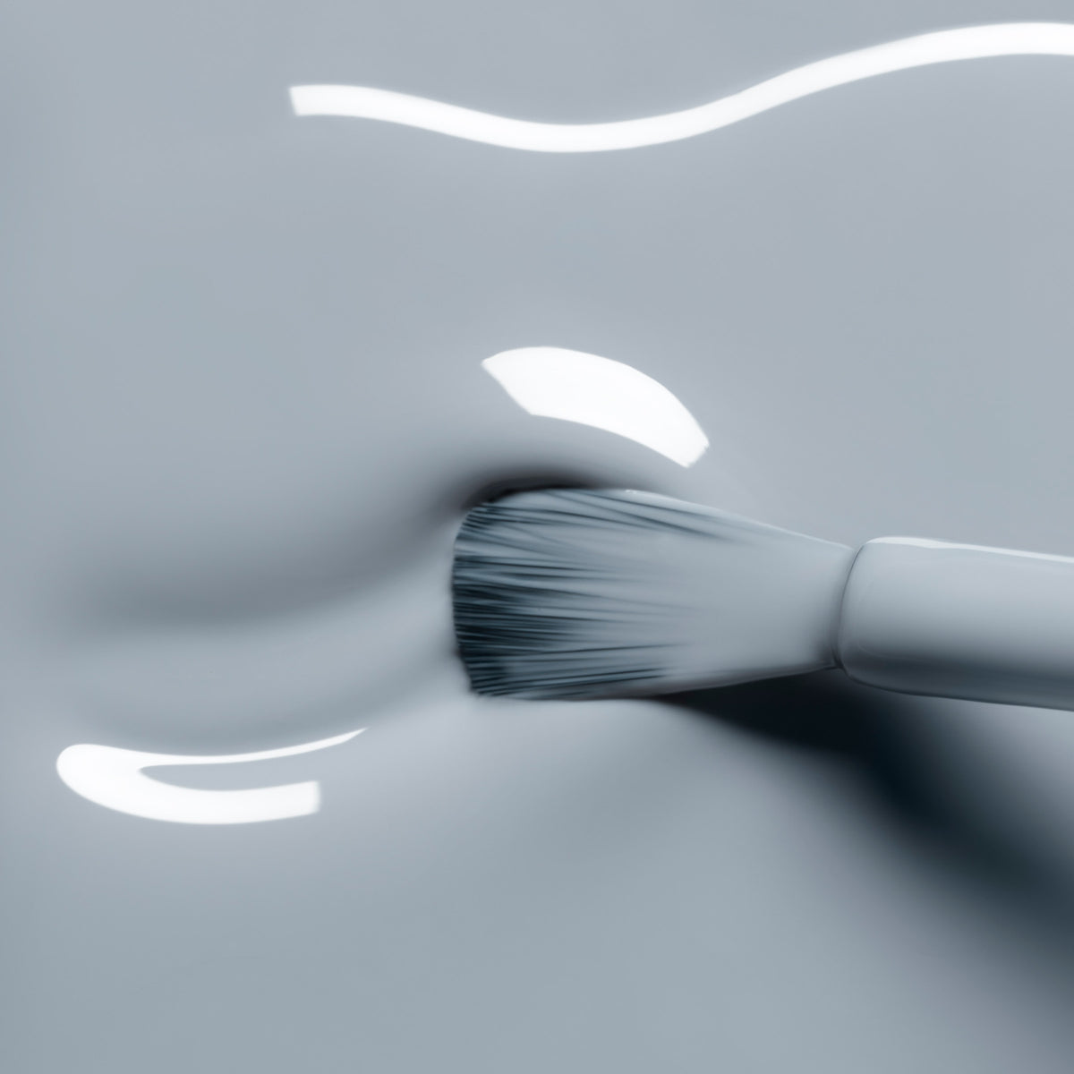 A close-up of a brush spreading Manucurist Mist Grey gel polish—its glossy, light gray shade shines with smooth, reflective texture.