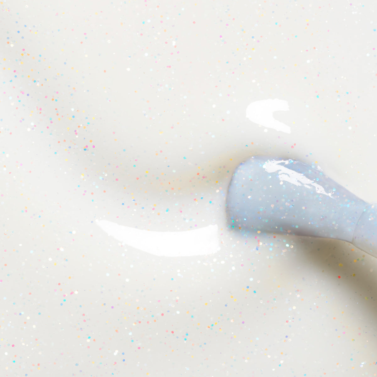 Gros plan sur le pinceau de vernis Nebula de Manucurist appliquant un vernis blanc laiteux à paillettes multicolores sur une surface lisse, révélant un fini brillant effet holographique avec des particules scintillantes éparses.