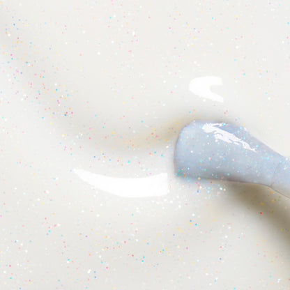 Close-up of Manucurist’s Nebula nail polish brush applying milky white polish with multicolored glitter on a smooth surface, revealing a glossy, holographic-like finish with scattered sparkling specks.