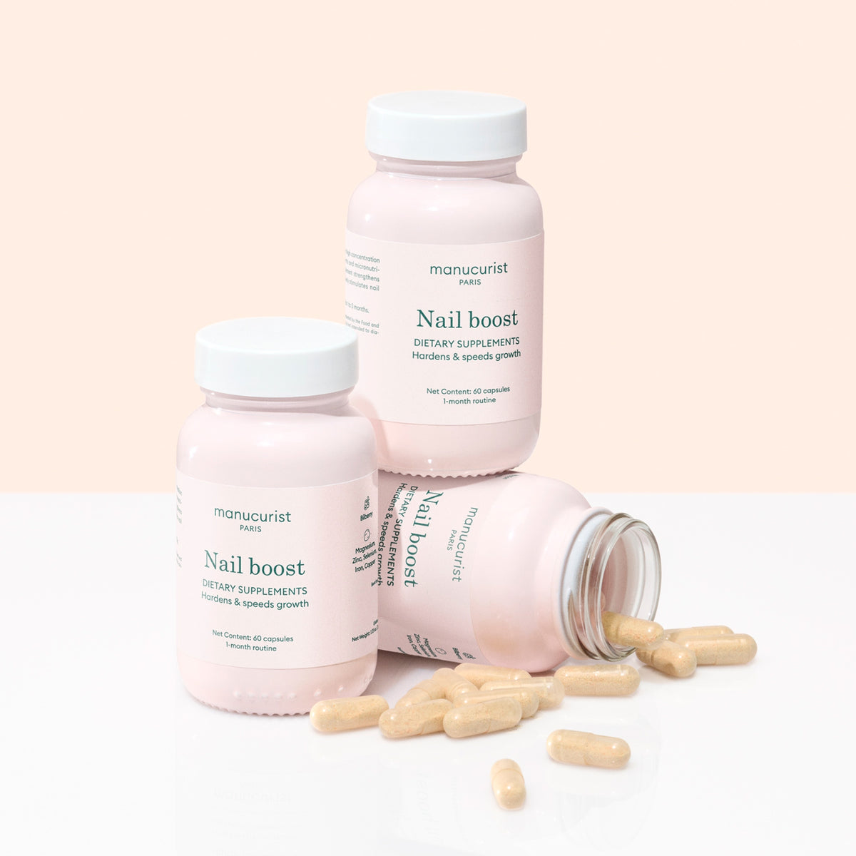 Trois flacons de compléments Nail Boost de Manucurist sont disposés sur une surface claire, dont un couché sur le côté avec des gélules beiges renversées, mettant en avant le soutien à la croissance des ongles et des ongles plus forts.
