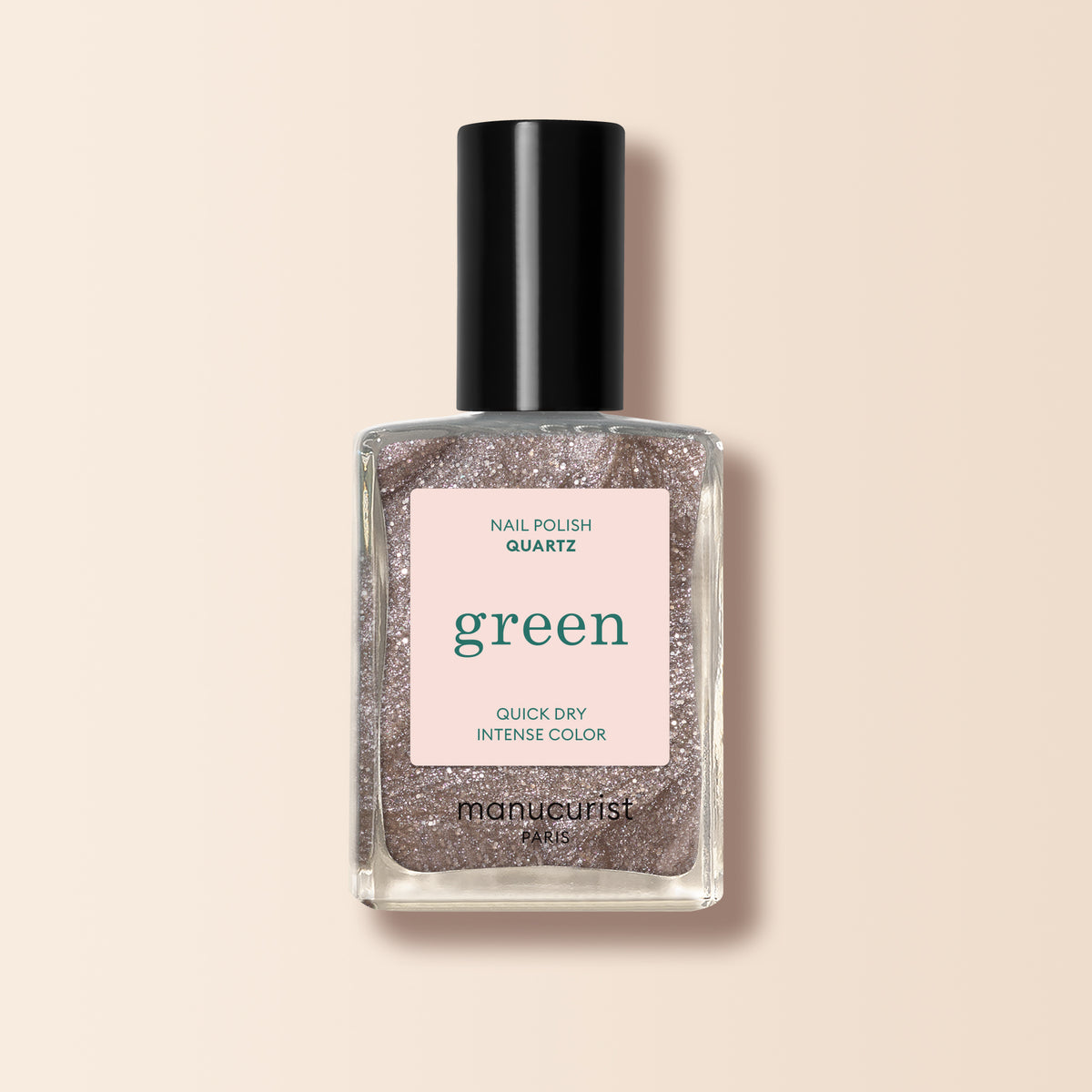 A clear bottle of Manucurist Quartz nail polish with a black cap, showcasing a shimmery light rose gold hue labeled “green” and “quick dry intense color” on a soft beige background.