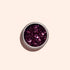 Un pot rond et ouvert de paillettes biodégradables Manucurist Bordeaux est placé au centre sur un fond rose pâle ; ses grosses paillettes magenta captent la lumière et reflètent des nuances de rose et de violet.