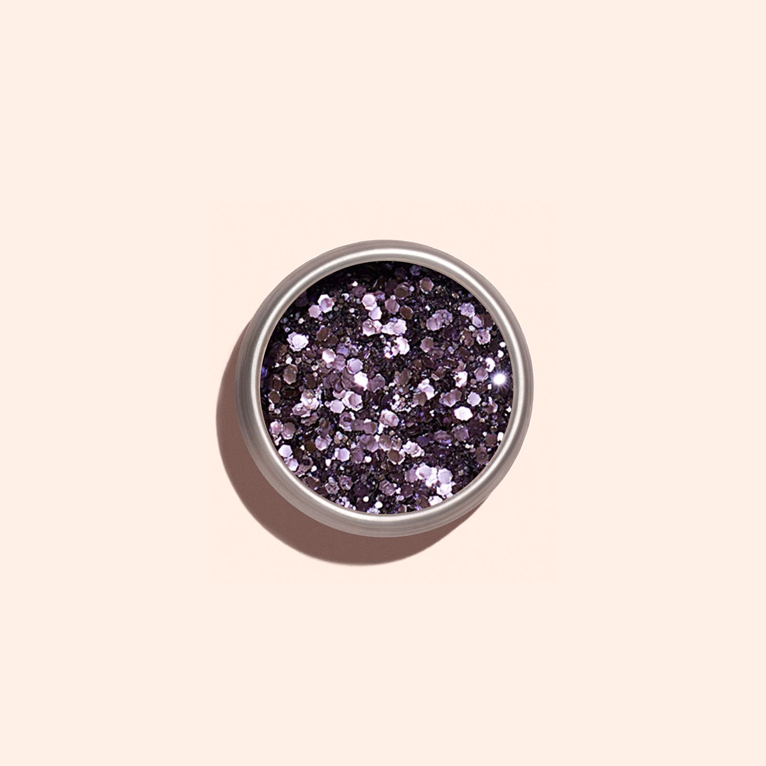A small round container of Manucurist Lilac Biodegradable Glitter, featuring chunky, reflective mauve particles for nail art, sits on a light beige background and casts a soft shadow.