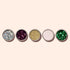 Cinq pots ronds de paillettes biodégradables Biodegradable Holo Glitter de Manucurist — argent, violet, or, rose pâle et vert — contenant des poudres scintillantes pour un Nail Art créatif, soigneusement disposés sur un fond beige clair.