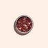 Un petit pot rond de Glitter biodégradable Pink Quartz de Manucurist, rempli de grosses paillettes rose gold brillantes, est posé sur un fond beige clair — parfait pour ajouter une touche d’éclat éco-responsable à votre Nail Art.
