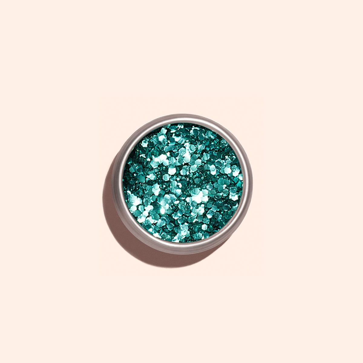 A small round container of Manucurist Turquoise Biodegradable Glitter rests on a plain light beige background, ready to enhance your nail art or gel polish designs.