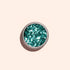 A small round container of Manucurist Turquoise Biodegradable Glitter rests on a plain light beige background, ready to enhance your nail art or gel polish designs.