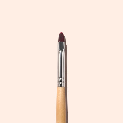 A single Manucurist Flat Brush with a wooden handle and brown bristles is vertically centered on a plain, light beige background, making it ideal for precise manicure and cuticle care.