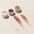 Trois pots ouverts des Trios de paillettes et poudres à effets Manucurist — blanc, or rose et or — sont posés sur une surface claire, avec des swatches scintillants assortis présentés devant.