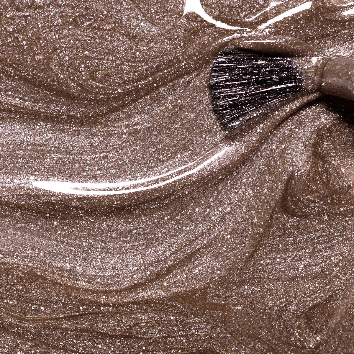 A close-up of the Manucurist Quartz brush swirling through shimmery, metallic bronze makeup, creating smooth, sparkling patterns reminiscent of glossy brown nail polish.