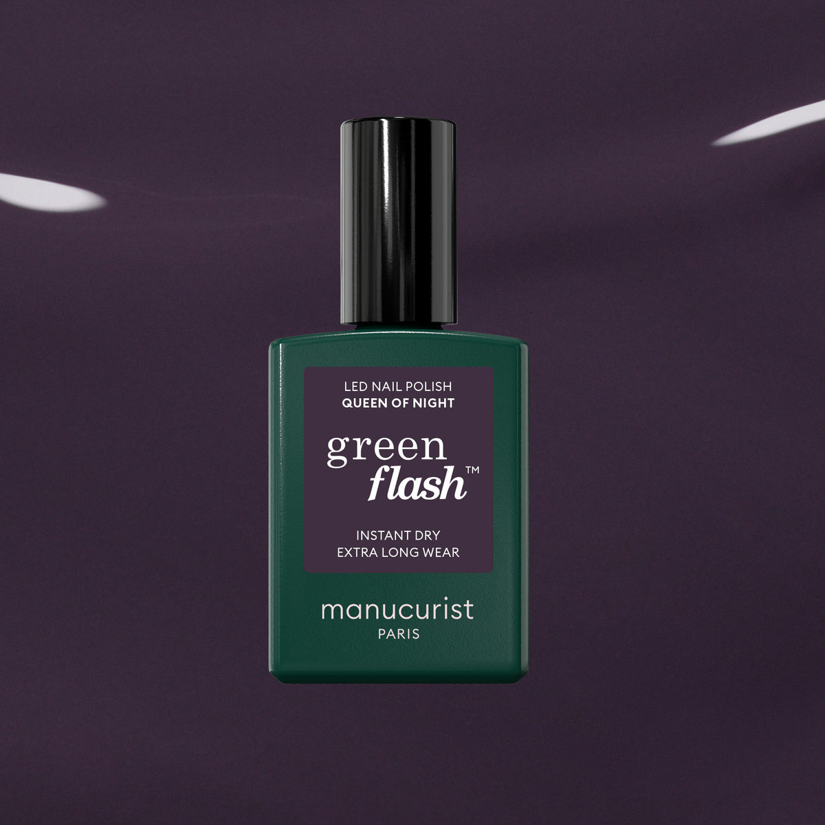 A dark green Manucurist Queen of Night nail polish bottle rests against a glossy purple backdrop, highlighting its gray undertones and unique style.
