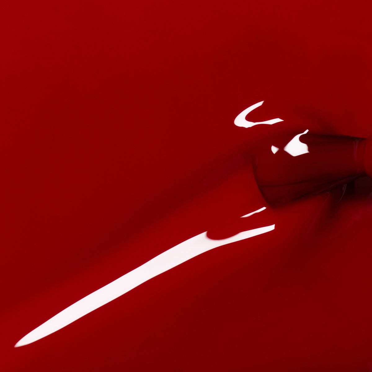 A close-up of Manucurist Red Velvet gel polish being poured, forming a smooth, glossy surface with a reflective sheen and a streak of white light.
