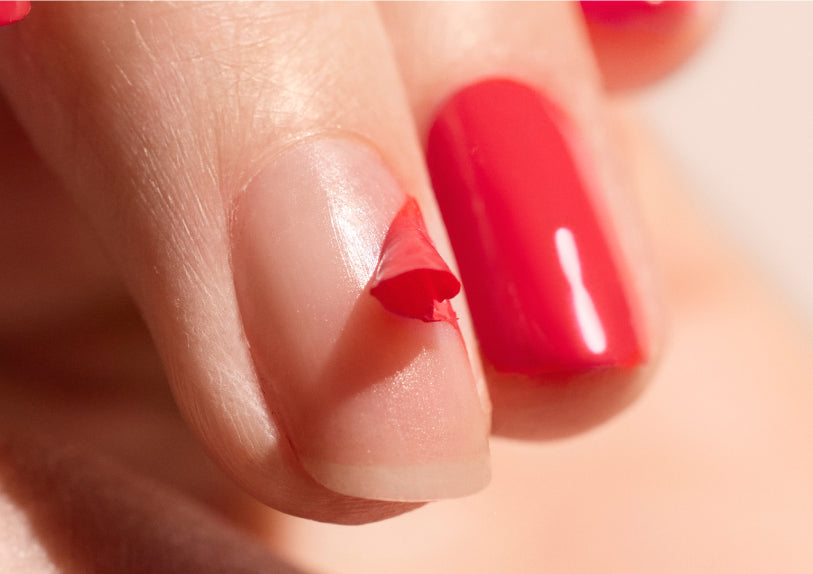Gros plan sur une main avec du vernis à ongles rouge, montrant un ongle où le vernis s'écaille, révélant l'ongle naturel en dessous.