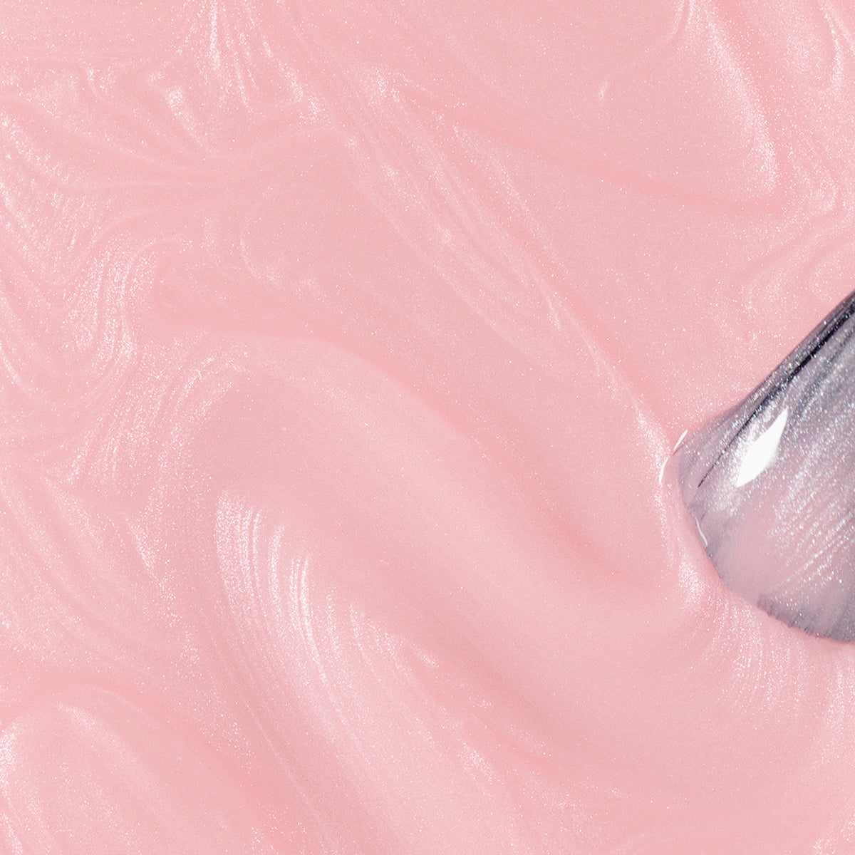 A close-up of a metallic spatula spreading Satin, a glossy, pearlescent light pink nail polish by Manucurist, in swirling patterns across a flat surface.