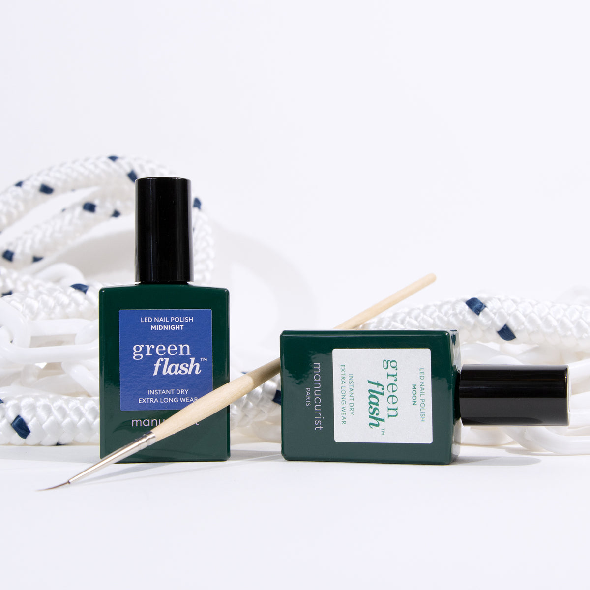 Deux flacons de vernis à ongles Manucurist Midnight Swim sont présentés avec un bâtonnet repousse-cuticules en bois, devant une corde blanche enroulée aux détails bleu marine sur fond blanc, idéale pour un nail art créatif.