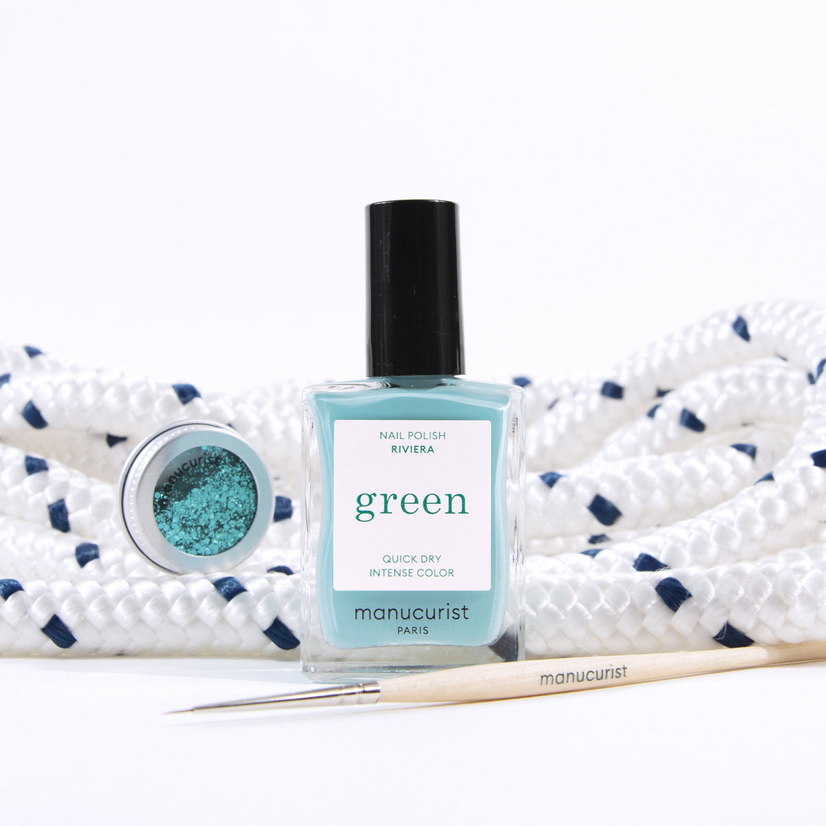 Un flacon de vernis à ongles Manucurist Underwater Glitter est posé devant une corde blanche enroulée avec des touches bleu marine, accompagné d&